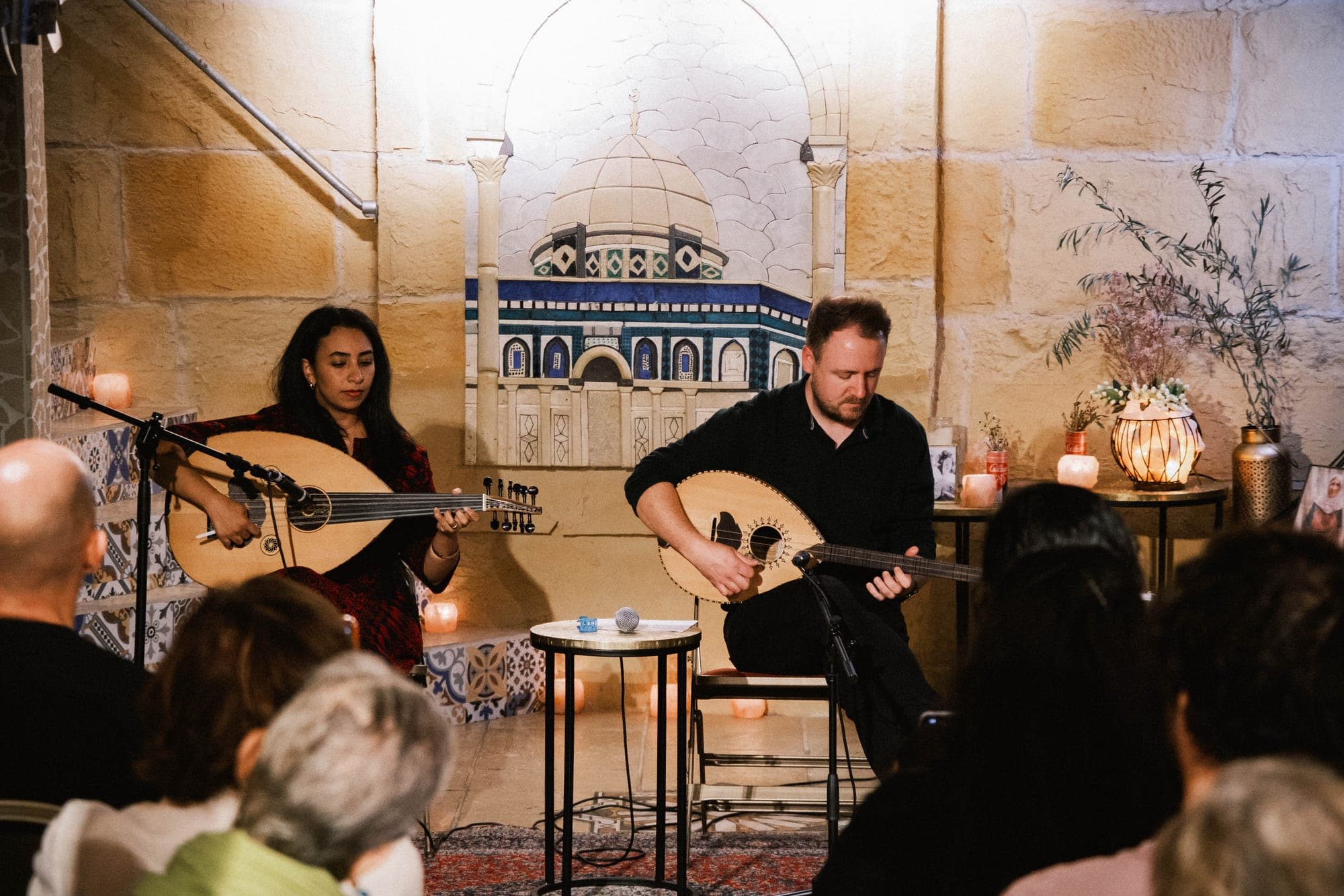 Two musicians playing the oud on a candlelit stage.